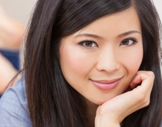 A person with long dark hair resting their chin on their hand, wearing a blue top.